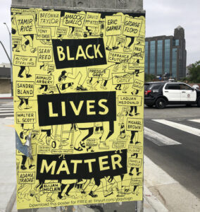 A large poster that says "BLACK LIVES MATTER" over a background of illustrated legs marching alongside the names of Black Americans killed by police or in police custody