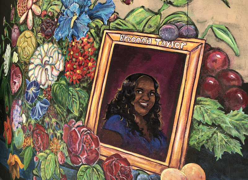 A mural of a smiling Breonna Taylor in a gold frame nestled in a bed of colors in numerous hues.