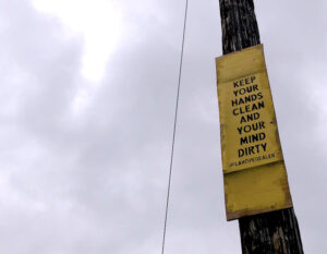 A sign attached high on a telephone pole reads "Keep your hands clean and your mind dirty"