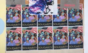 Posters of essential workers (doctors, nurses, construction, security, maintenance, retail) in front of a U.S. flag wearing masks, with the word SOLIDARITY underneath.
