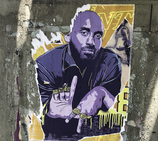 A poster of Kobe Bryant in purple and gold, holding his fingers to form the letters L.A. with championship rings on his fingers