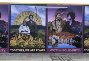 Wall size images featuring photographs of indigenous and Black women side by side, collaged into natural landscapes, with the text underneath "TOGETHER, WE ARE POWER" and "VOTE IN SOLIDARITY". (Artwork by Mer Young.)
