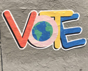 A giant sticker says VOTE in multiple colors with a globe in the middle of the O.