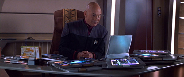 Jean Luc Picard sits at a desk covered in tablet devices